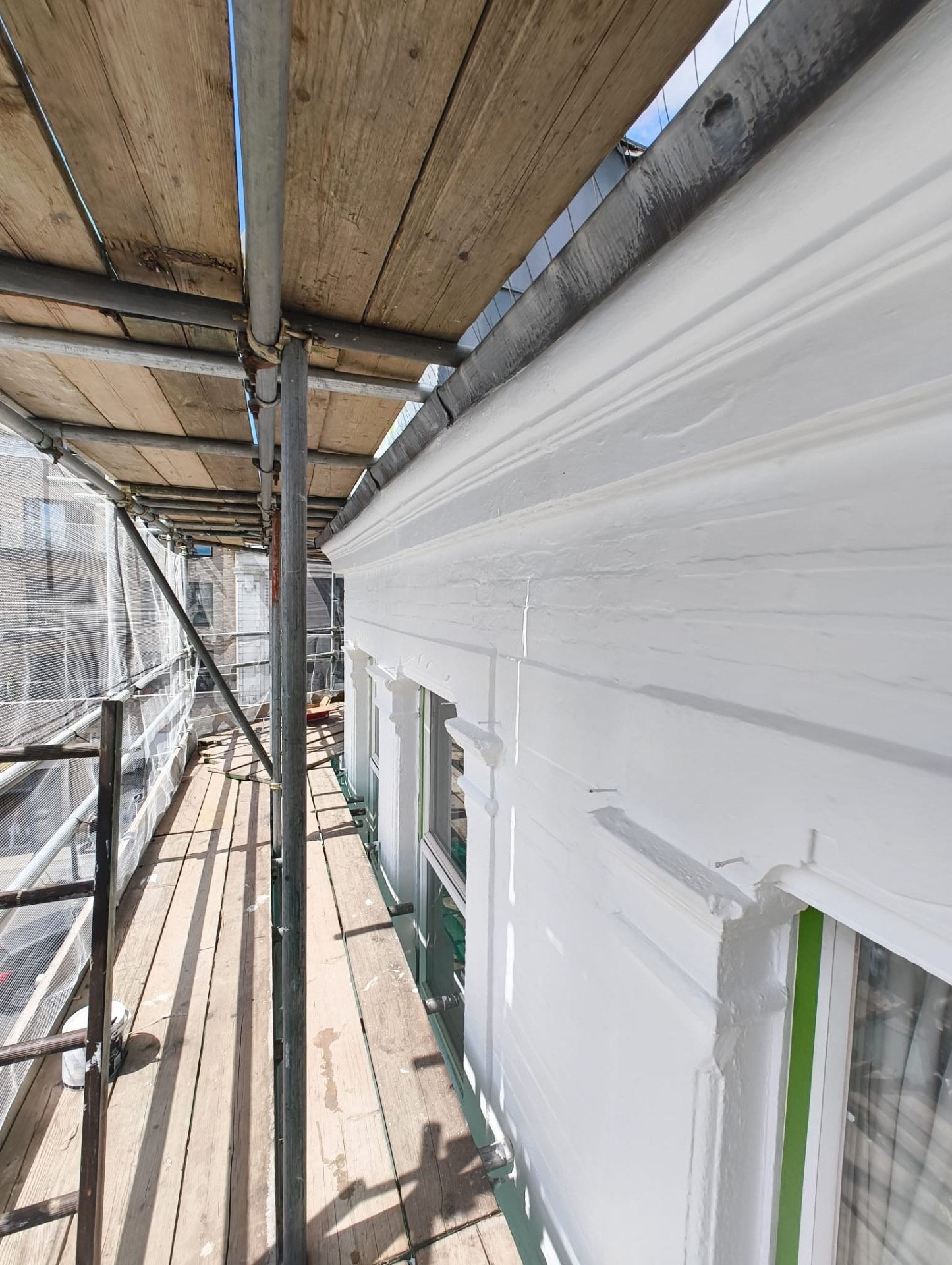 Newly painted parapet and gutter line seen along the scaffold walkway