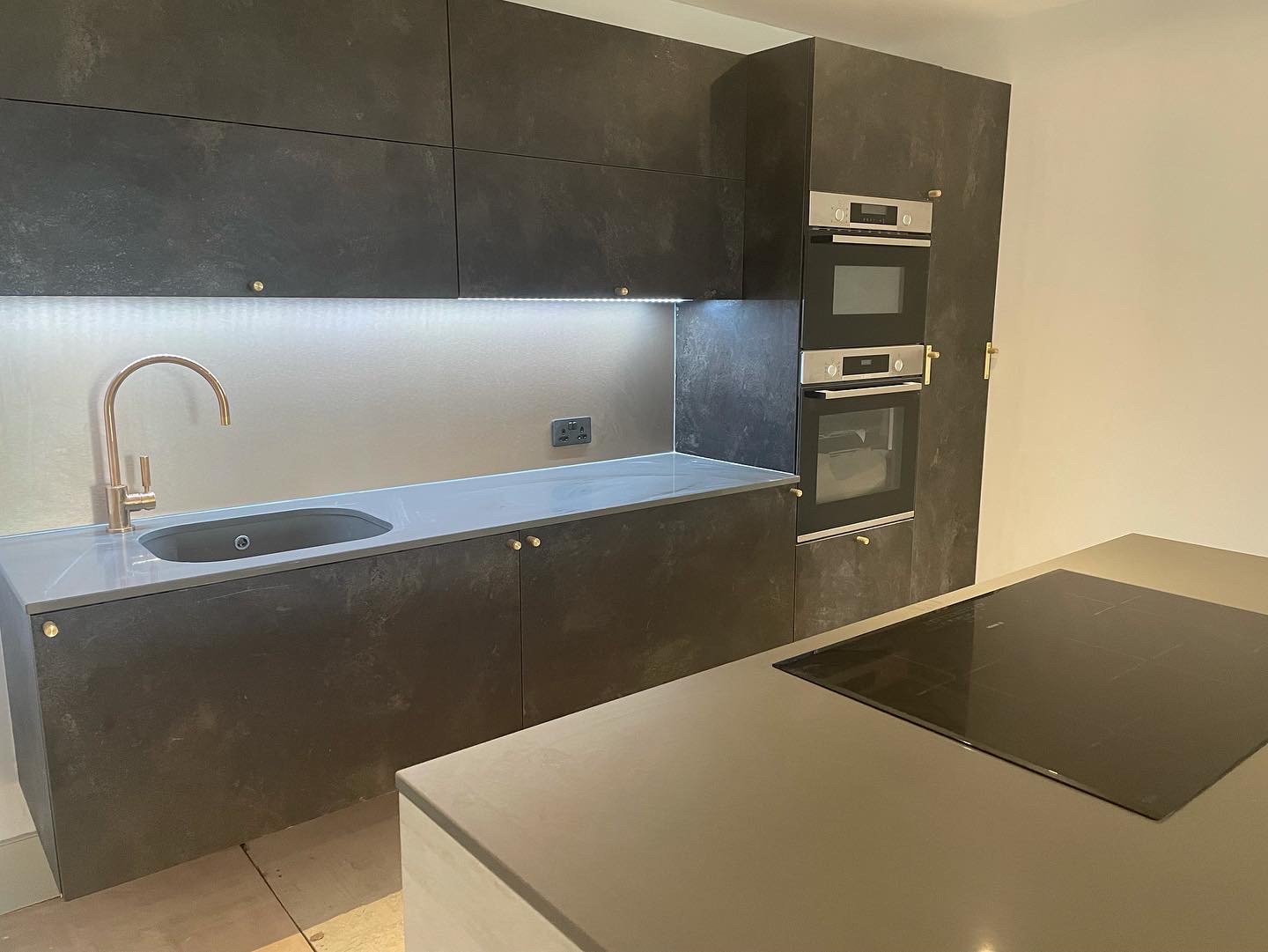 Dark fitted cabinetry, grey worktops and central induction hob