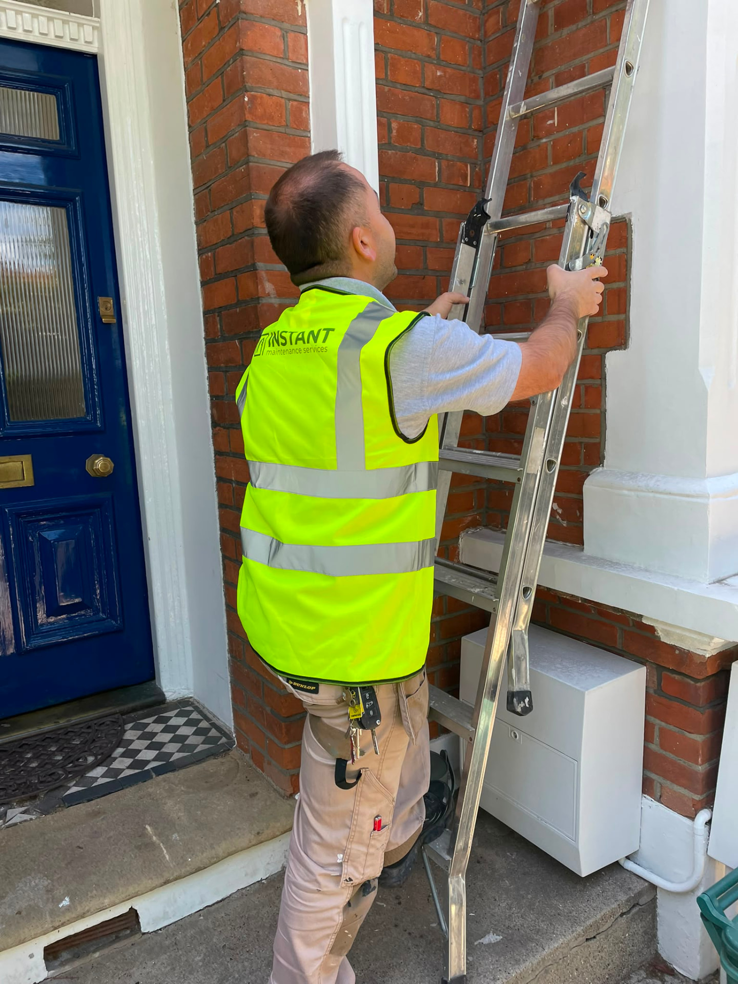 IMS engineer in branded high visibility workwear setting a ladder against a period London property